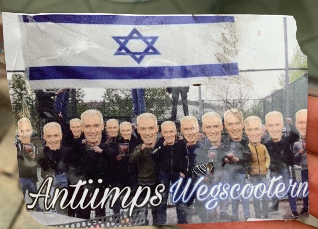 A long Israel flag over a crowd of figures in streetwear, their faces plastered over with identical images of a smiling man with bleached short hair. “Antiimps wegscootern” or “Scooter away the anti-imperialists.”