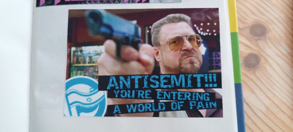 A screen capture from the film The Big Lebowski, showing the character of Vietnam vet and recent Jewish convert Walter Sobchak pointing a pistol. “ANTISEMITE! YOU’RE ENTERING A WORLD OF PAIN”.